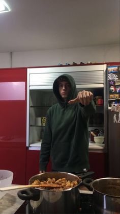 a man in a hoodie pointing at the camera while standing next to a pot full of food