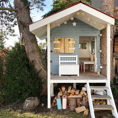 a small blue and white house sitting next to a pile of firewood in front of a tree