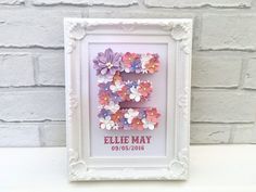 the letter e is made out of paper flowers in a white frame on a shelf