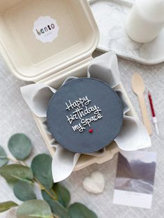 a happy birthday cookie in a box on a table next to some flowers and candles