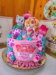 a pink cake with paw patrol characters on top and decorations around the edges, sitting on a table