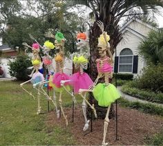 skeleton statues in colorful tutu skirts and headdresses are lined up against a tree