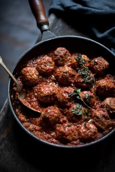 meatballs with tomato sauce and herbs in a skillet on a wooden table, ready to be eaten