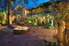 an outdoor patio with fire pit surrounded by greenery and trees at night, in front of multi - story building