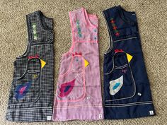 three children's vests are lined up on the floor, one has an applique