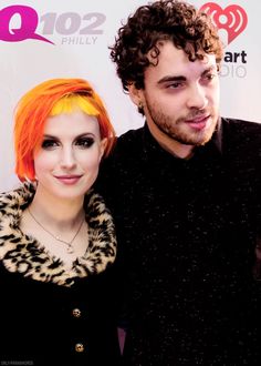 a man standing next to a woman with bright orange hair and black dress at an event