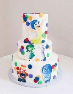 a three tiered birthday cake decorated with cartoon characters and polka dot decorations on a white table