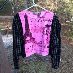 a pink shirt with black and white designs hanging on a clothes rack in front of trees