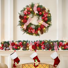 christmas decorations and stockings hanging from a mantel with a wreath on the wall behind it