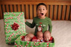 a young boy sitting in a bed next to two baby babies wearing green christmas sweaters