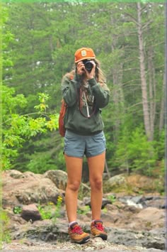 a woman standing on top of a rock next to a forest filled with green trees