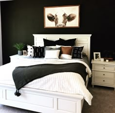 a bedroom with black walls and white bedding is pictured in this image, there are two nightstands on either side of the bed