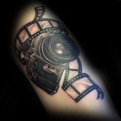 a black and white tattoo with a camera on it's arm, in the shape of a film strip