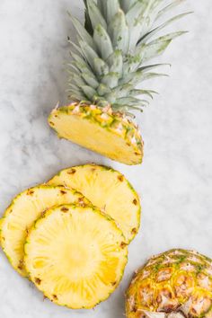 a pineapple sliced in half next to a whole pineapple on a marble surface