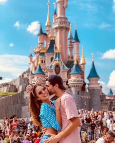 a man and woman standing in front of a castle with lots of people around it