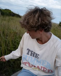 a young man sitting on top of a cement slab next to a cow in a field