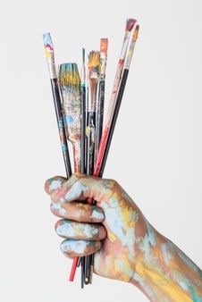 a person's hand holding several paint brushes in front of their face and body