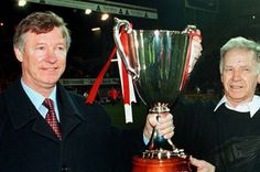 two men standing next to each other holding up a trophy