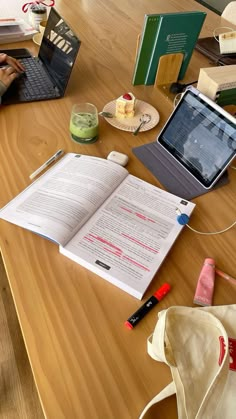 an open book sitting on top of a wooden table next to a laptop and other items