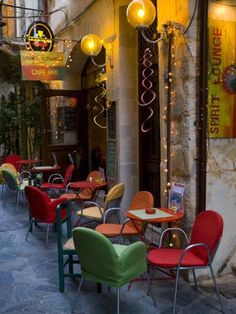 tables and chairs are lined up on the side walk in front of a building with lights hanging from it