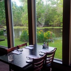 the table is set for four in front of large windows overlooking a pond and grassy area