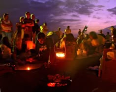 a group of people sitting around a campfire at night with the sun shining on them