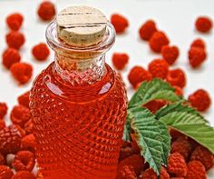 a glass bottle filled with raspberries next to green leaves