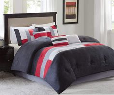 a bed with red and black comforters in a room next to a lamp on a table