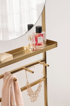 a gold shelf with a mirror, perfume bottle and necklaces on it in front of a window