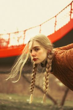 a woman with long blonde hair standing in front of a red bridge and looking at the camera