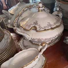 a table topped with lots of white and gold dishes covered in saucers, plates and bowls