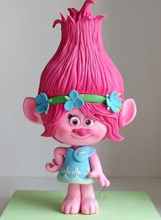 a pink troll with blue flowers on her head and hands, standing in front of a white wall