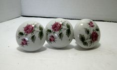 three white vases with pink roses painted on them sitting on a counter top next to each other