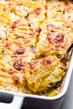 a casserole dish with potatoes and cheese in a white baking dish topped with a serving spoon