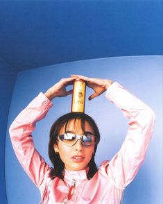 a woman in pink shirt and sunglasses holding up a bottle with both hands on top of her head