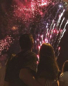 two people are looking at fireworks in the night sky with their arms around each other