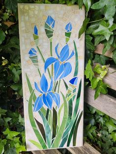 a painting on a wooden bench in front of green leaves and plants with blue flowers painted on it