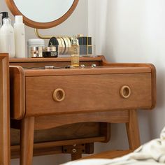 a wooden dresser sitting next to a bed with a round mirror on top of it