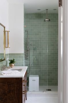 a bathroom with green tiles on the shower wall and white countertop, along with a wooden cabinet