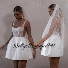 two women in white dresses and veils standing next to each other with their hands together