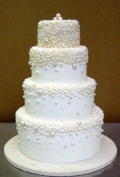 a three tiered white wedding cake with pearls