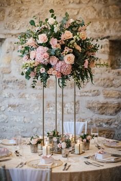 a table with flowers and candles on it in front of an old stone wall at a wedding reception