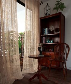 a table and chair in front of a window with sheer curtains