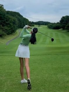 a woman is swinging her golf club at the green