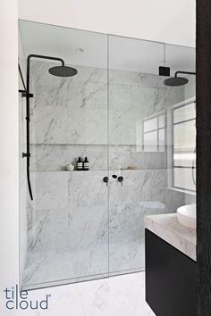 a bathroom with a glass shower door and white marble counter top, along with a sink