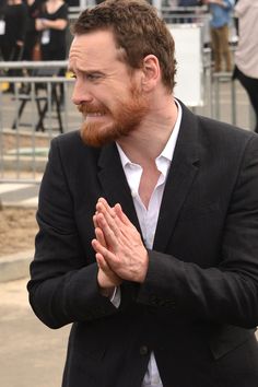 a man in a suit and white shirt is standing with his hands folded while looking off to the side