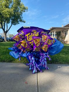 a bouquet of candy wrapped in purple and blue ribbon on the sidewalk next to a house