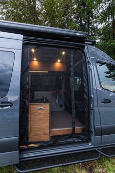 the inside of a van with its doors open and lights on in the trees behind it