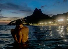 two people in the water at night with mountains in the background and lights reflecting on the water