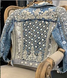 the back of a blue jean jacket with beading and pearls on it, sitting on a wicker chair